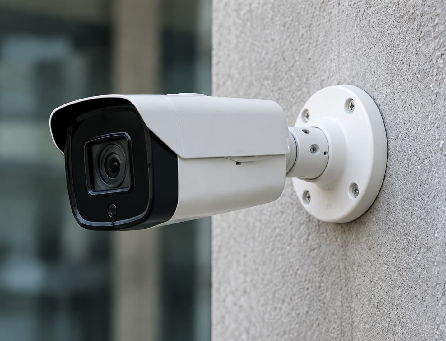A traditional analog CCTV box camera mounted on a concrete wall